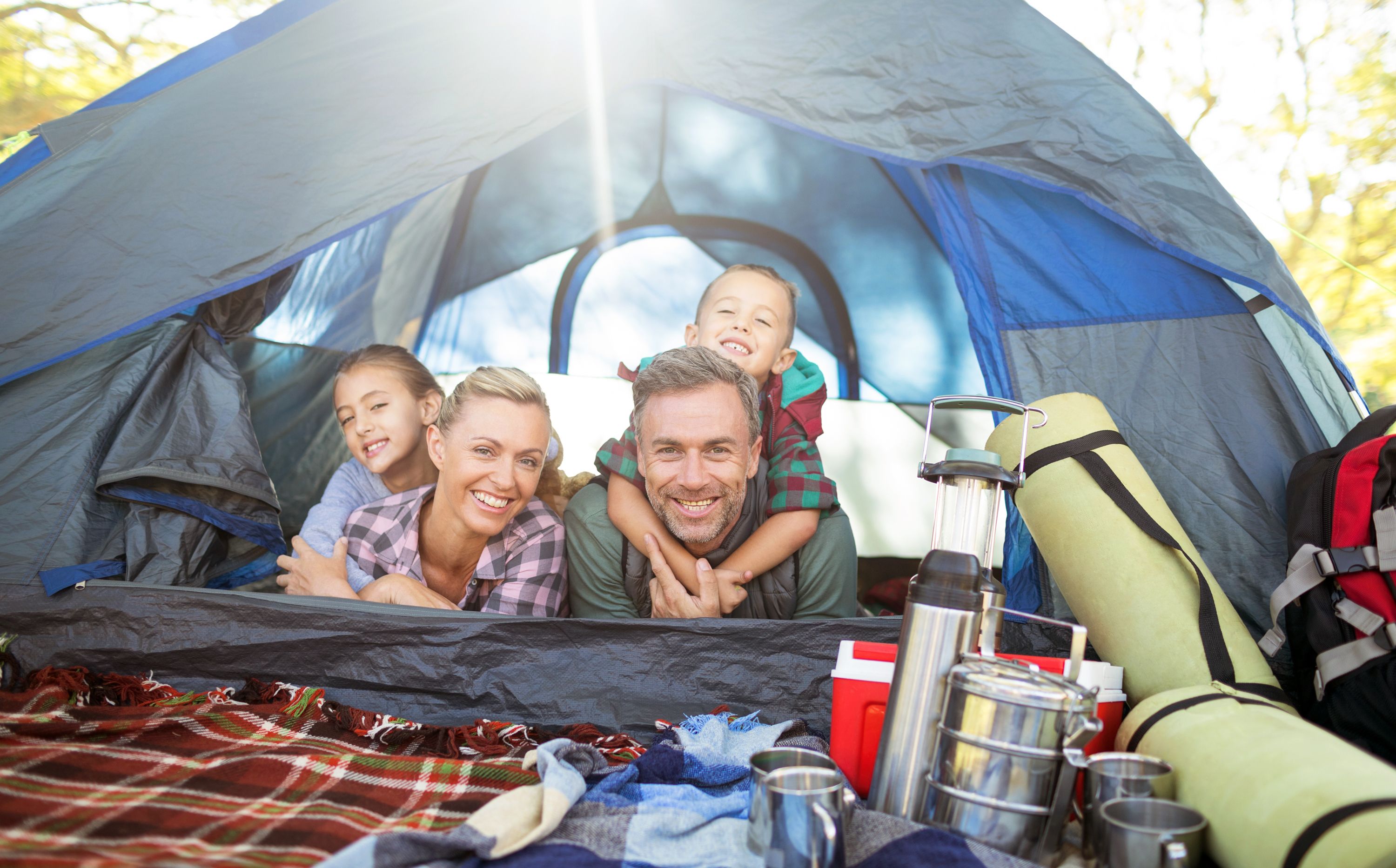 Familie liegt in einem Zelt mit allerlei Campingausrüstung und schaut gemeinsam lachend hinaus