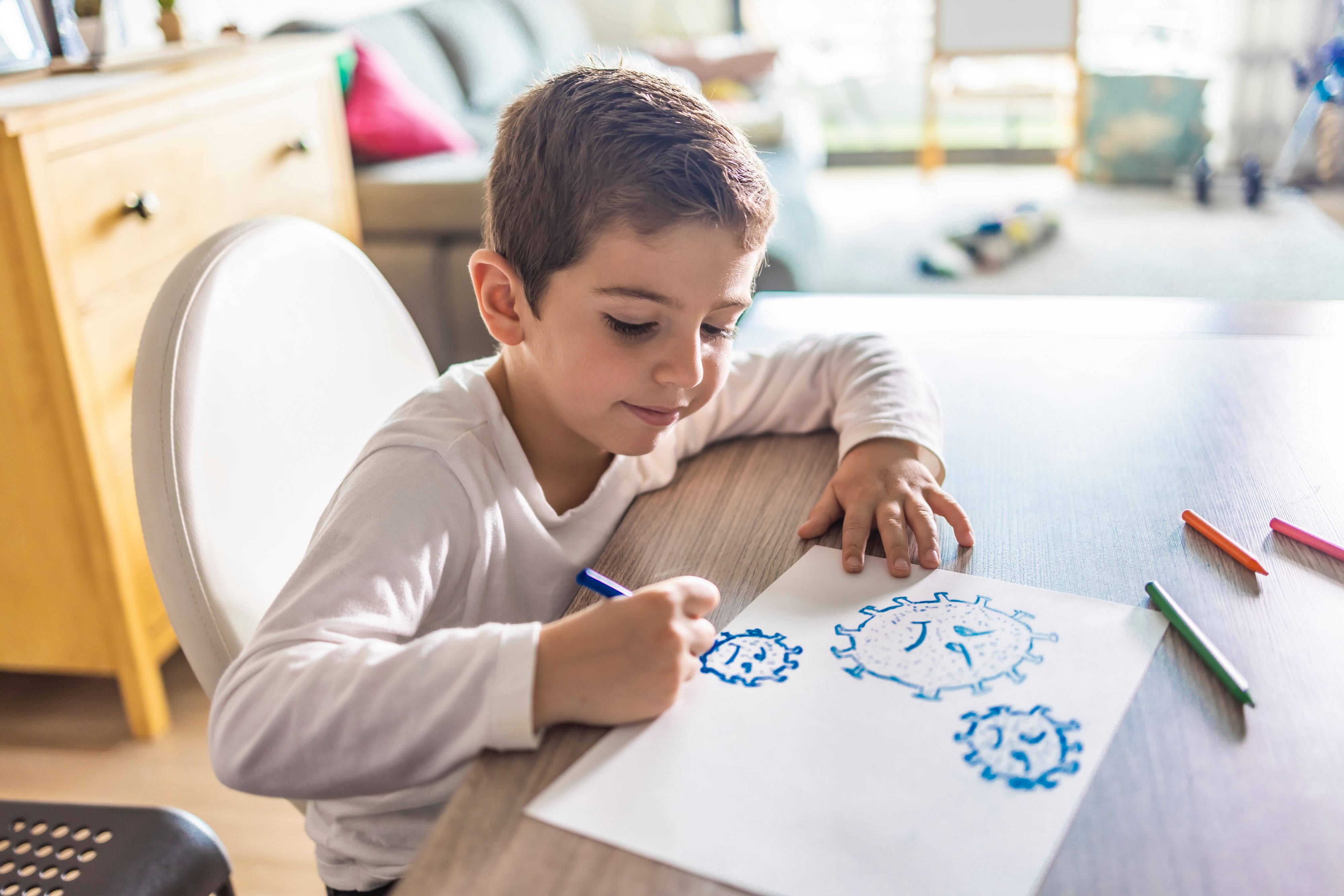 Kleiner Junge sitzt zu Hause am Tisch und malt auf einem Blatt Coronaviren