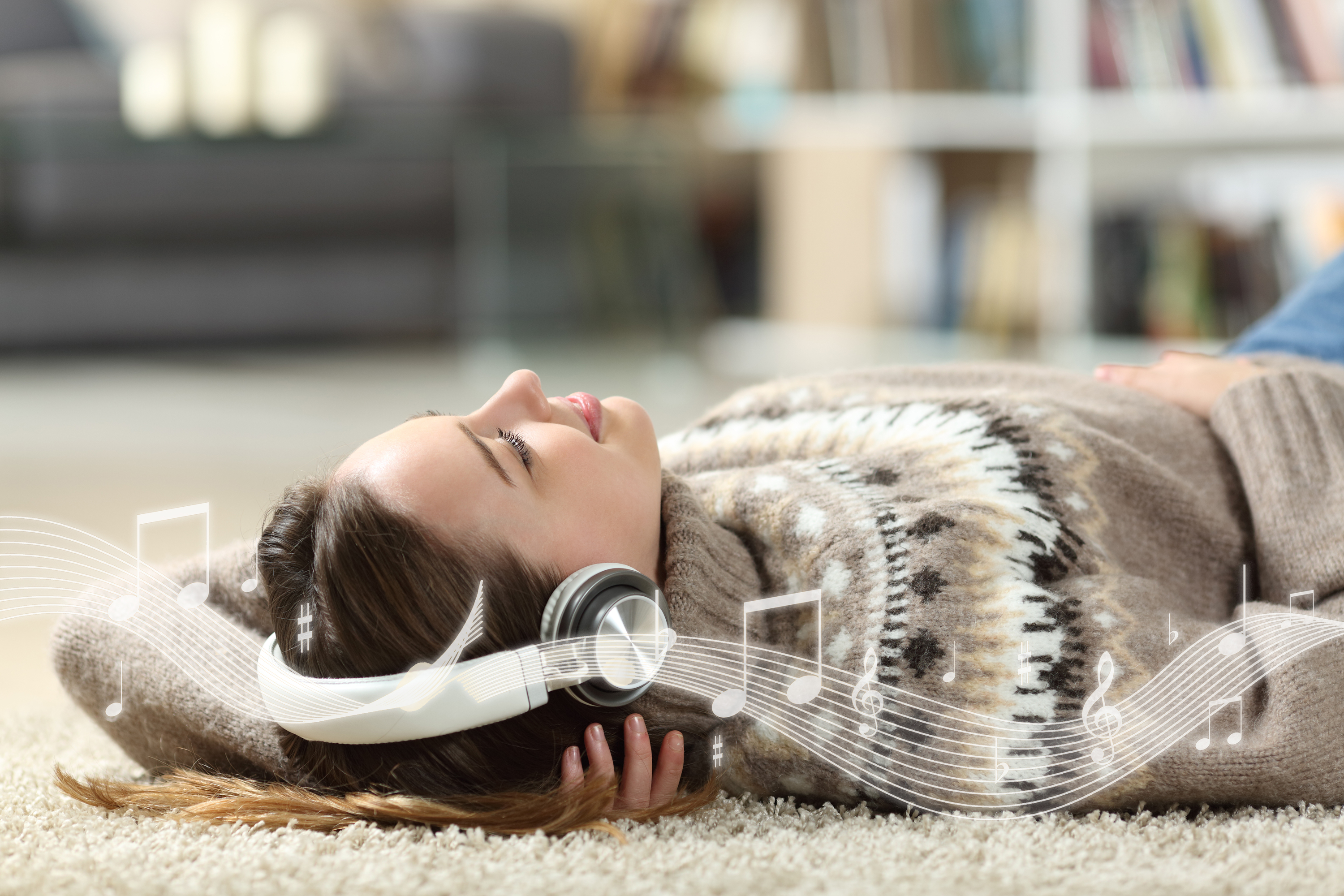 Frau mit Kopfhörern liegt auf einem Teppich und hört zufrieden ihre Lieblingsmusik