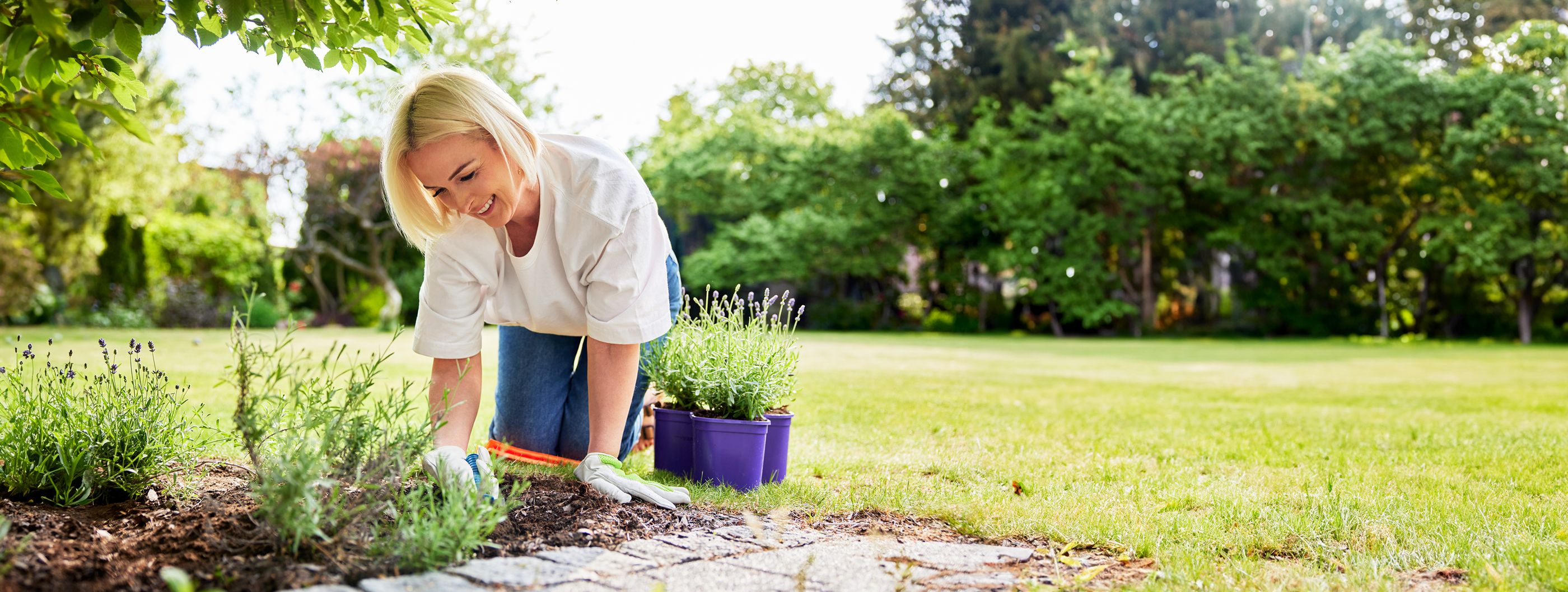 Frau kniet vor einem Beet auf dem rasen und verrichtet mit Freude Gartenarbeit